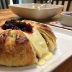 Golden baked Brie en Croûte served on a wooden platter with fresh fruit and crackers.