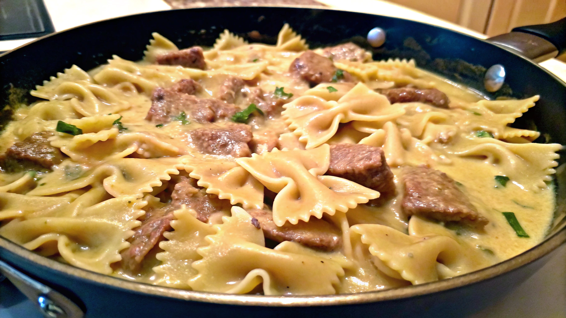 A plate of beef and bowtie pasta with creamy Alfredo sauce, garnished with fresh herbs